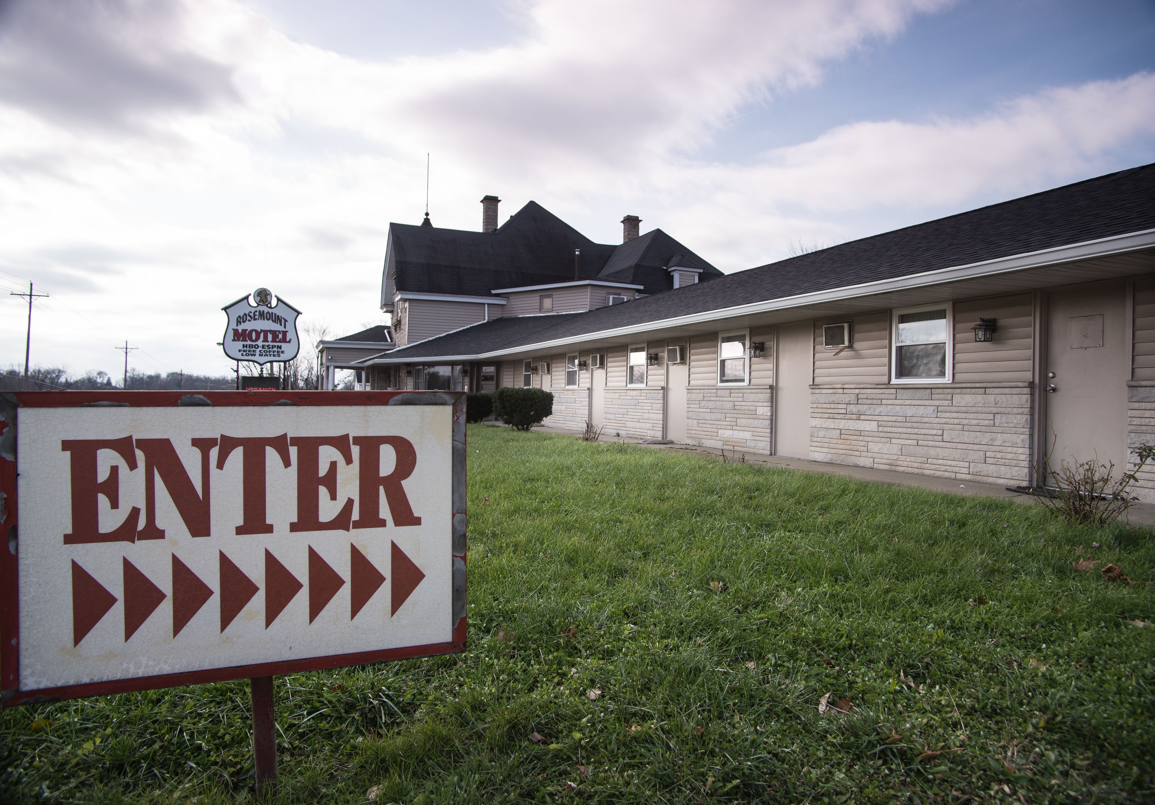 A motel sign with 'ENTER' and directional arrows, a large house with a garage, and a cloudy sky.