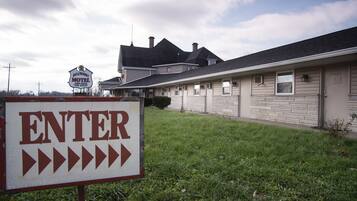 A motel sign with 'ENTER' and directional arrows, a large house with a garage, and a cloudy sky.