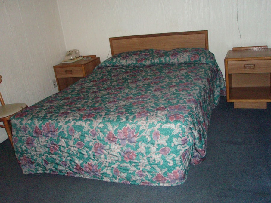 A standard hotel room with a single bed, a nightstand, a chair, and a wooden dresser.