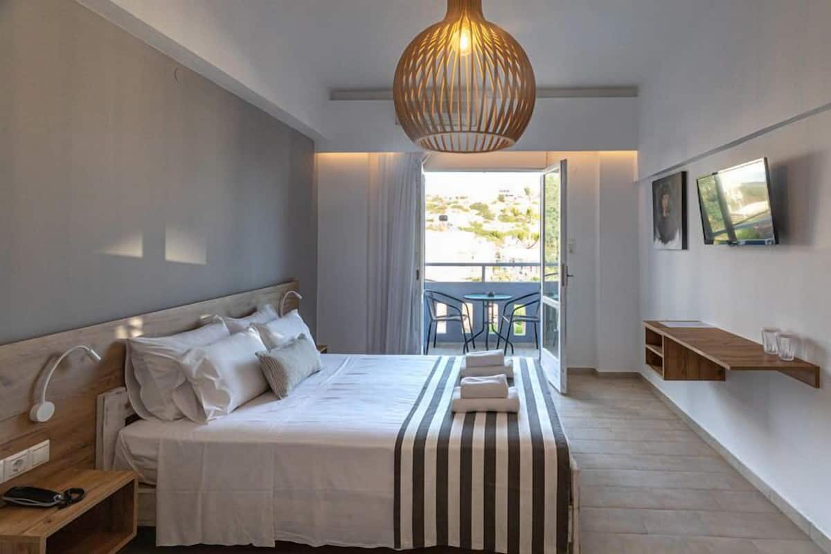 A modern hotel room with a large bed, a bedside table with a lamp, a wooden shelf, and a TV mounted on the wall.