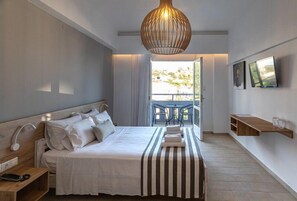A modern hotel room with a large bed, a bedside table with a lamp, a wooden shelf, and a TV mounted on the wall. - Triton Authentic Cretan Hotel (Minoa Pediada)