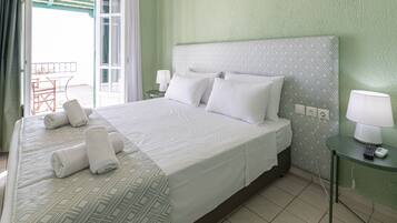 Una cama bien hecha con sábanas blancas y toallas enrolladas, una mesita de noche con lámpara y vistas a un patio al aire libre.