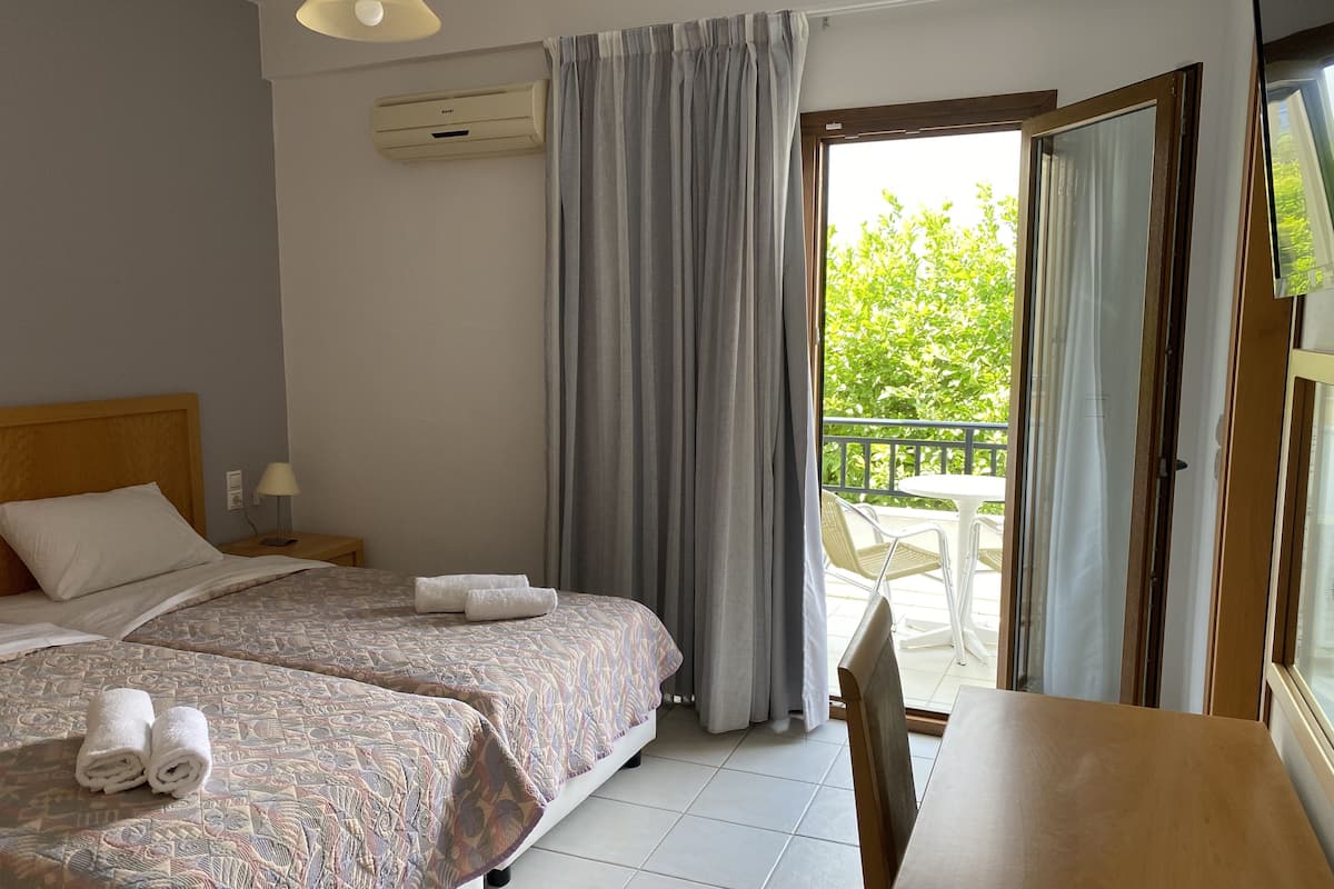 A hotel room with two beds, a table, and a balcony with outdoor furniture.