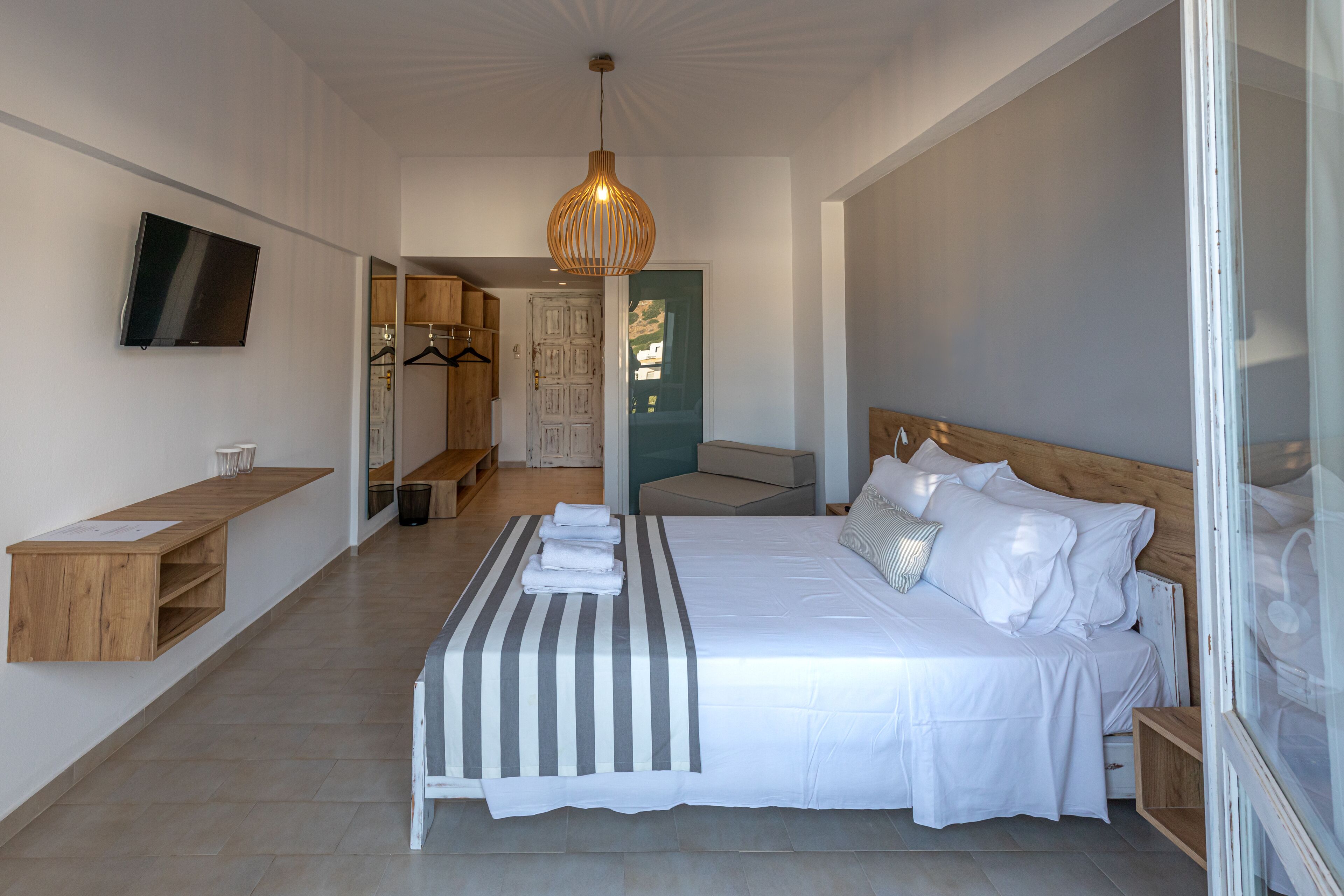 Une chambre à coucher moderne avec un grand lit, un téléviseur fixé au mur et une table de chevet en bois.