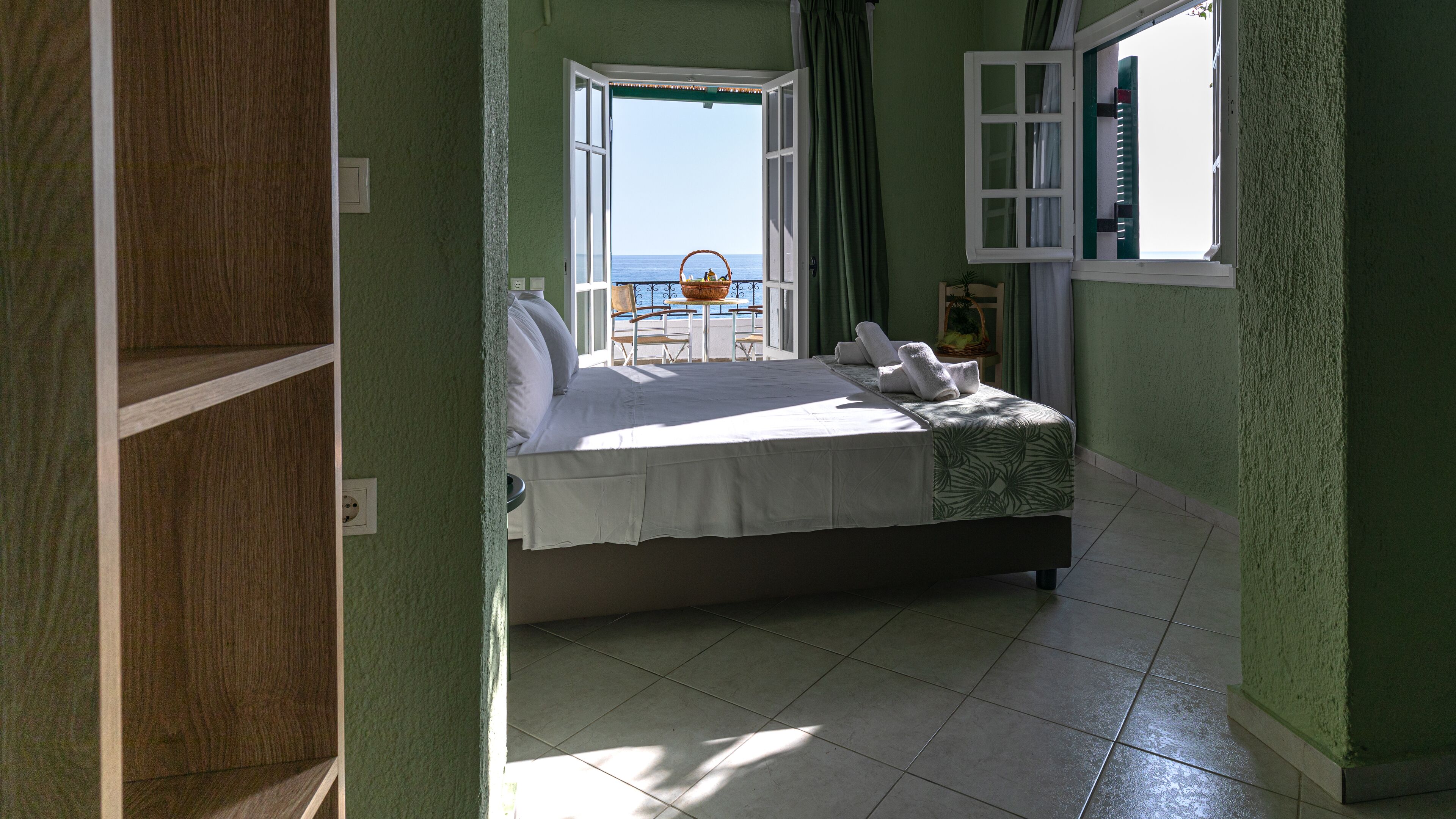 A bedroom with a bed, a view of the sea, and a window with curtains.