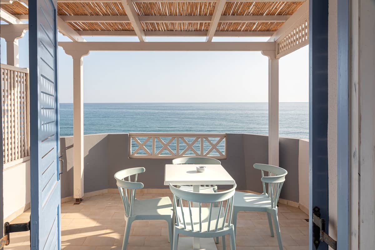 A covered outdoor seating area with a table and chairs, overlooking the sea.