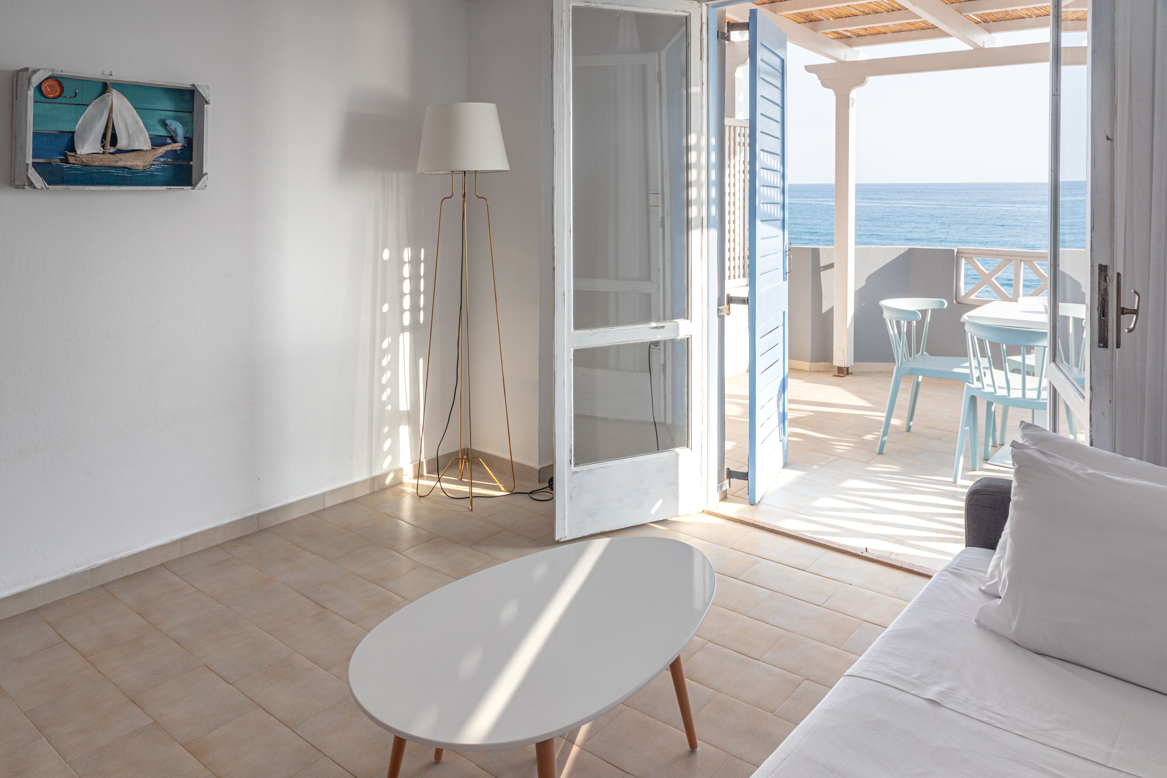 A room with a white sofa, a small white table, and a view of the sea through an open door.