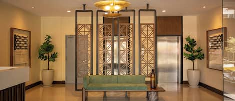 A reception area with a green sofa, a chandelier, potted plants, and a modern reception desk.
