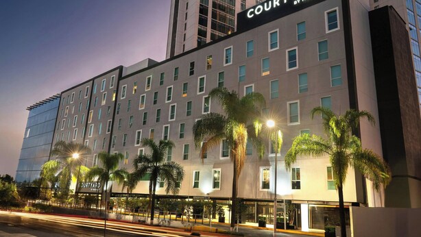 Ein Courtyard by Marriott Hotel mit mehreren Etagen, einer modernen Fassade und Palmen im Vordergrund.