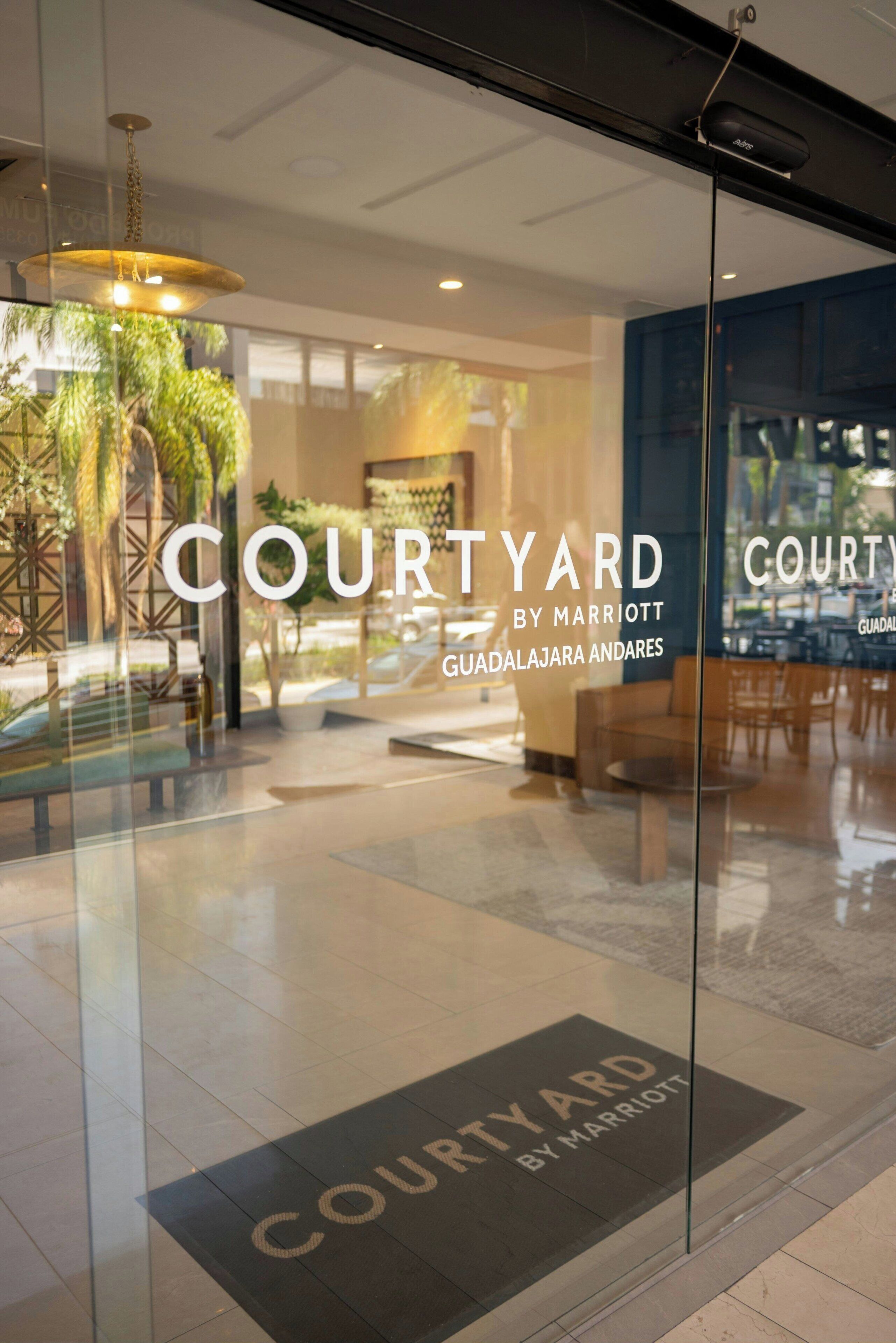 A glass entrance to a courtyard area with the text 'COURTYARD BY MARRIOTT GUADALAJARA ANDARES' visible.