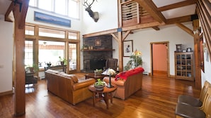 A spacious living room with wooden beams, a fireplace, and a mounted deer head. - Gallatin River Lodge (Bozeman)