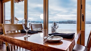 A dining table with chairs, a wooden table, and a view of a snowy landscape through large windows. - Gallatin River Lodge (Bozeman)