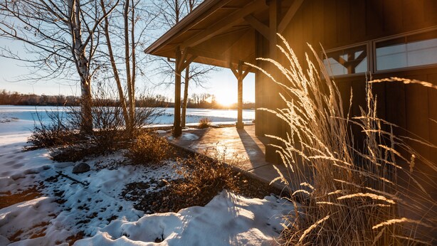 A wooden building with a covered patio overlooking a frozen lake. - Gallatin River Lodge (Bozeman)