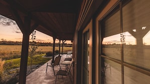 A covered patio with outdoor seating, a view of a field, and a building with large windows. - Gallatin River Lodge (Bozeman)