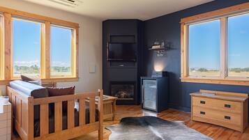 Una sala de estar moderna con un sofá de madera, chimenea, televisor y ventanas amplias con vistas al exterior.
