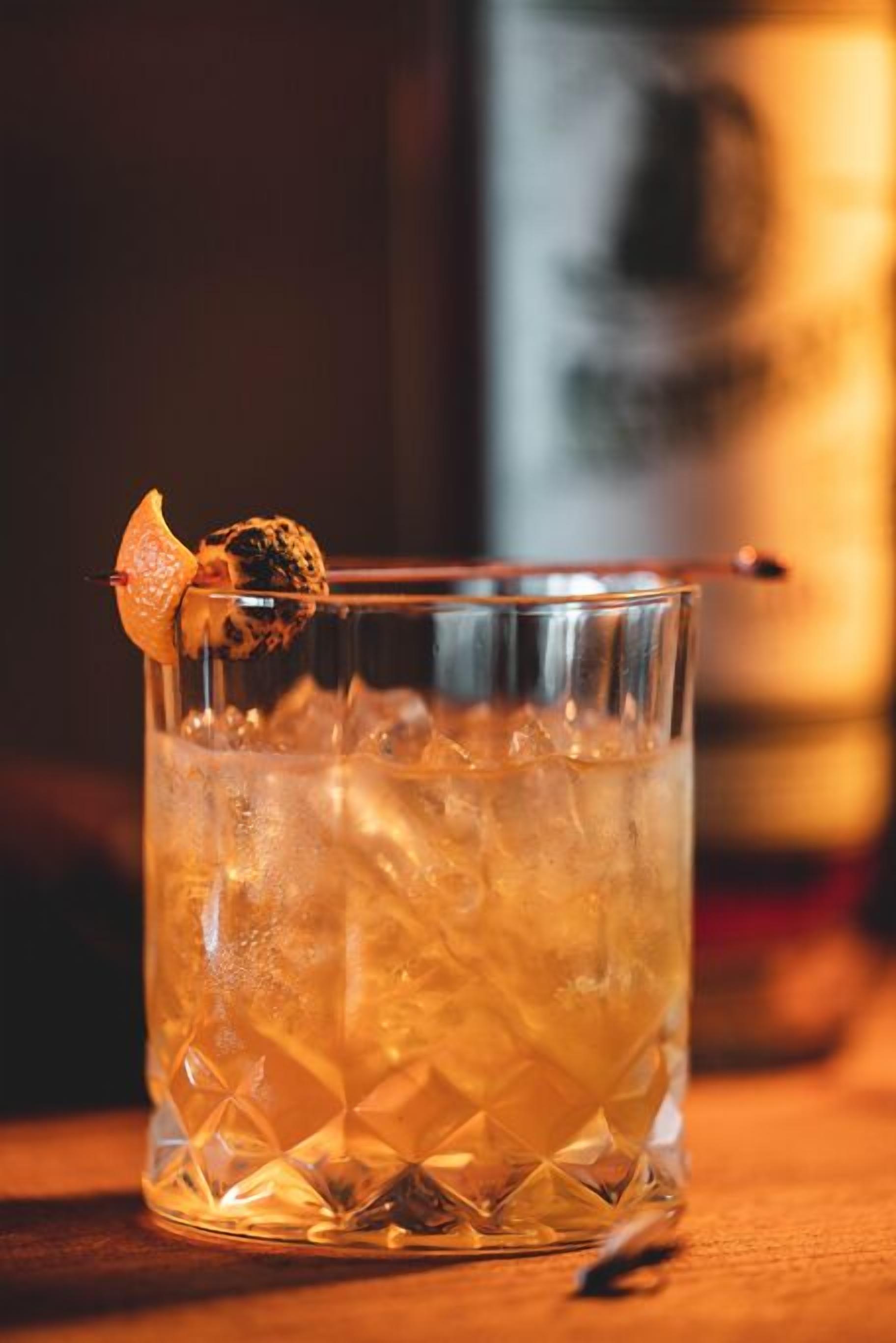 Ett glas med en cocktail, is och en dekoration på en träyta.