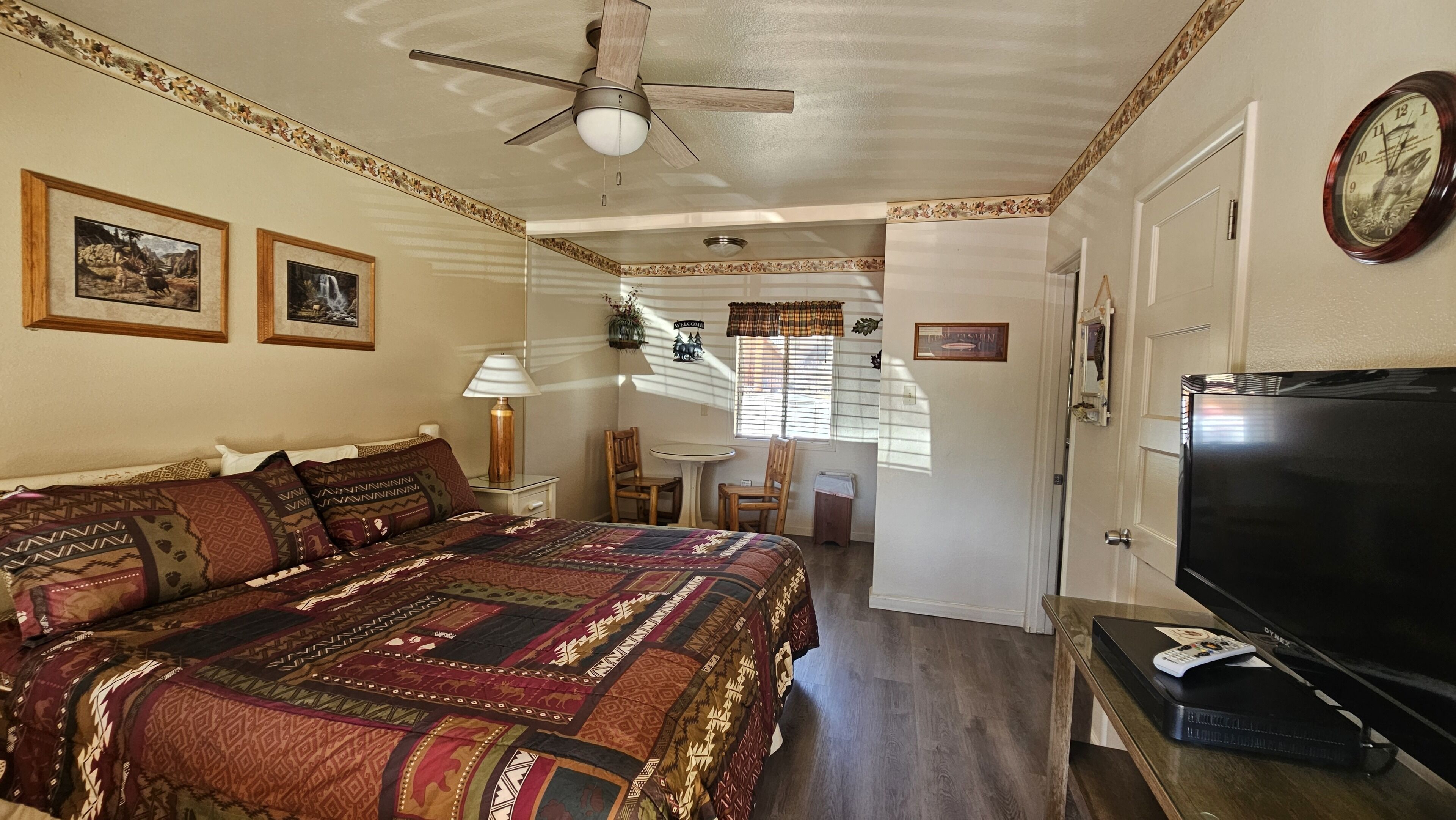 A bedroom with a large bed, a ceiling fan, a TV, and a small table with chairs.