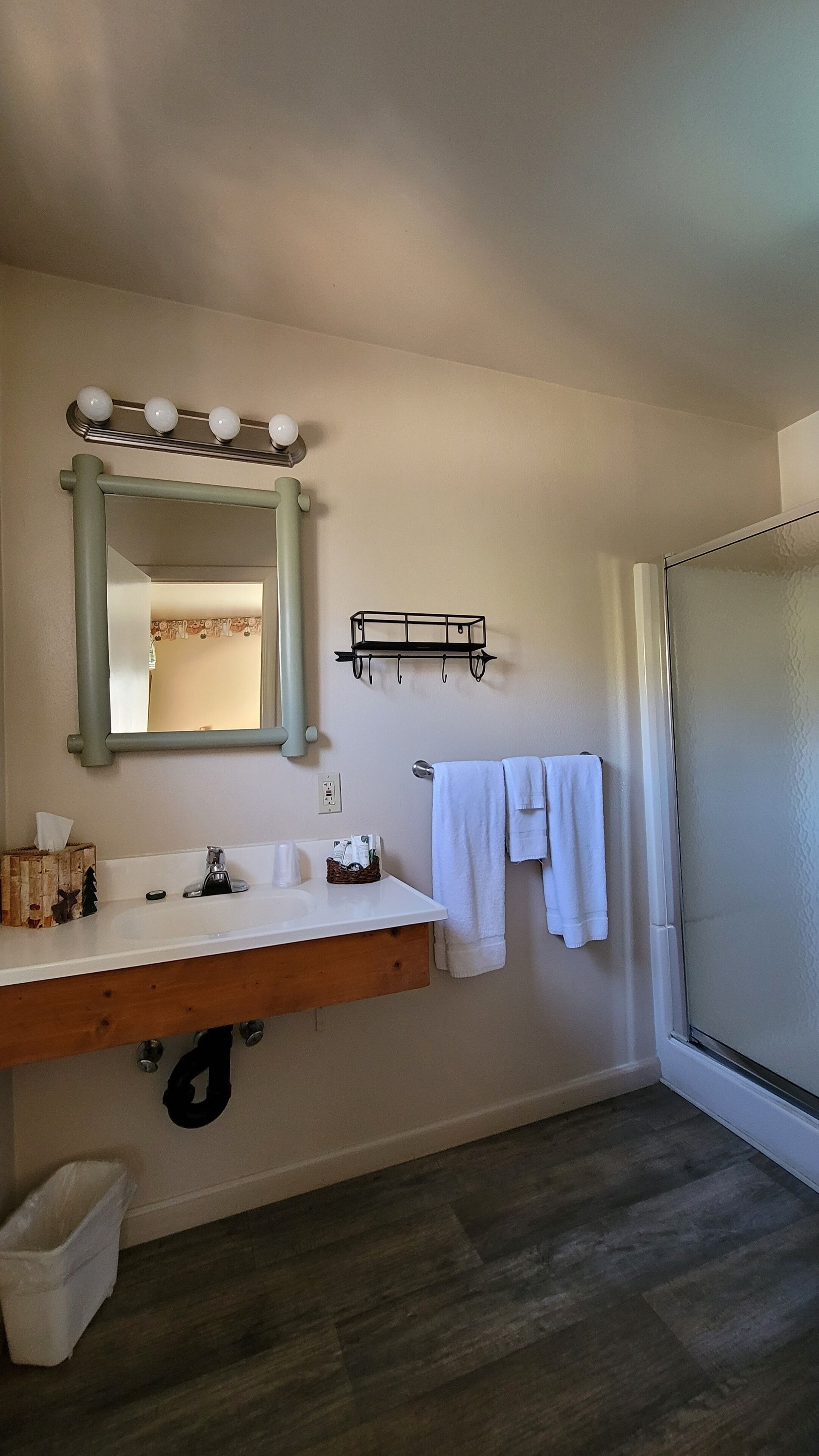A bathroom with a vanity, sink, mirror, towel rack, and a shower area.