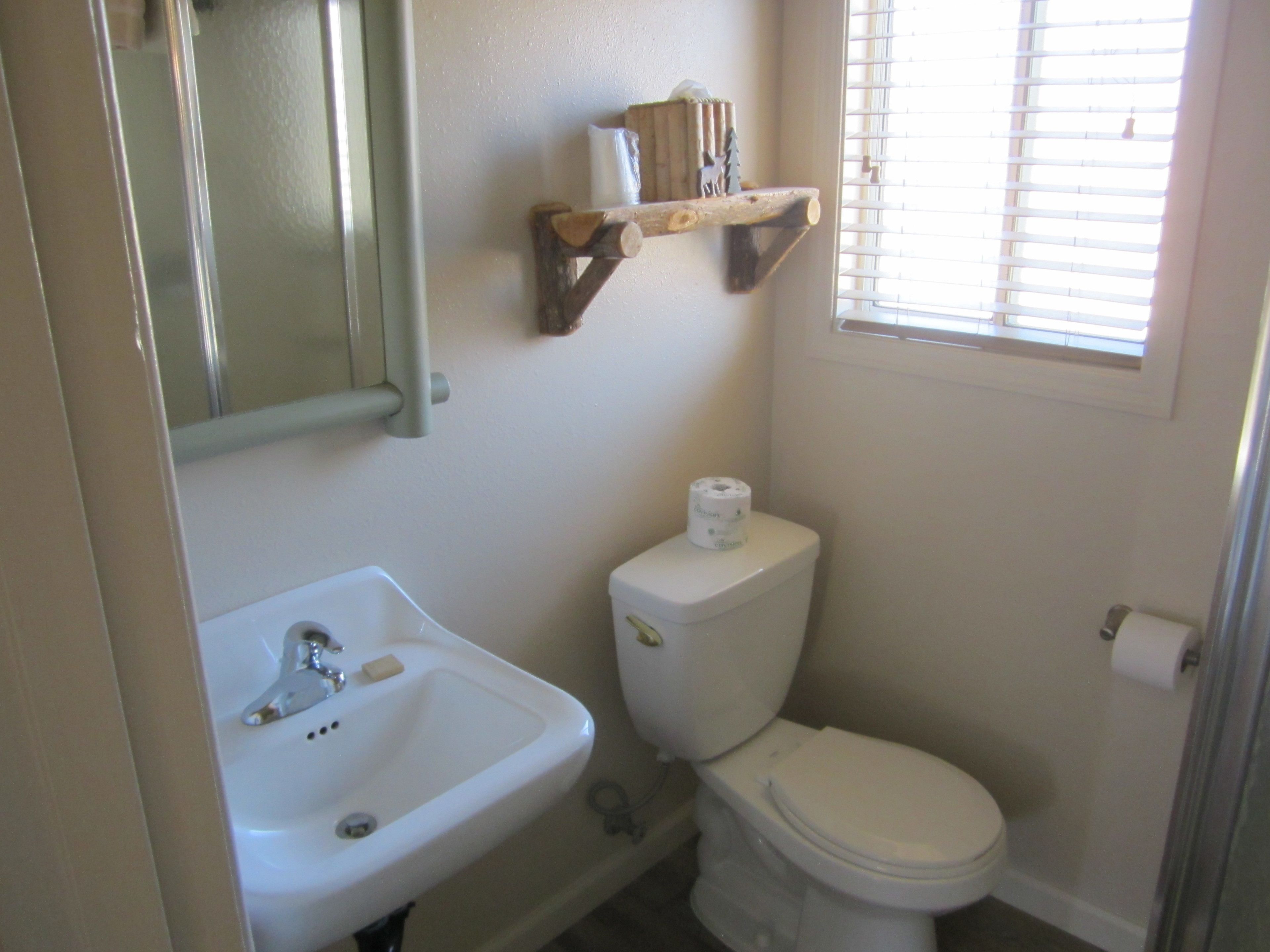 A bathroom with a white sink, toilet, and a shelf above the toilet.