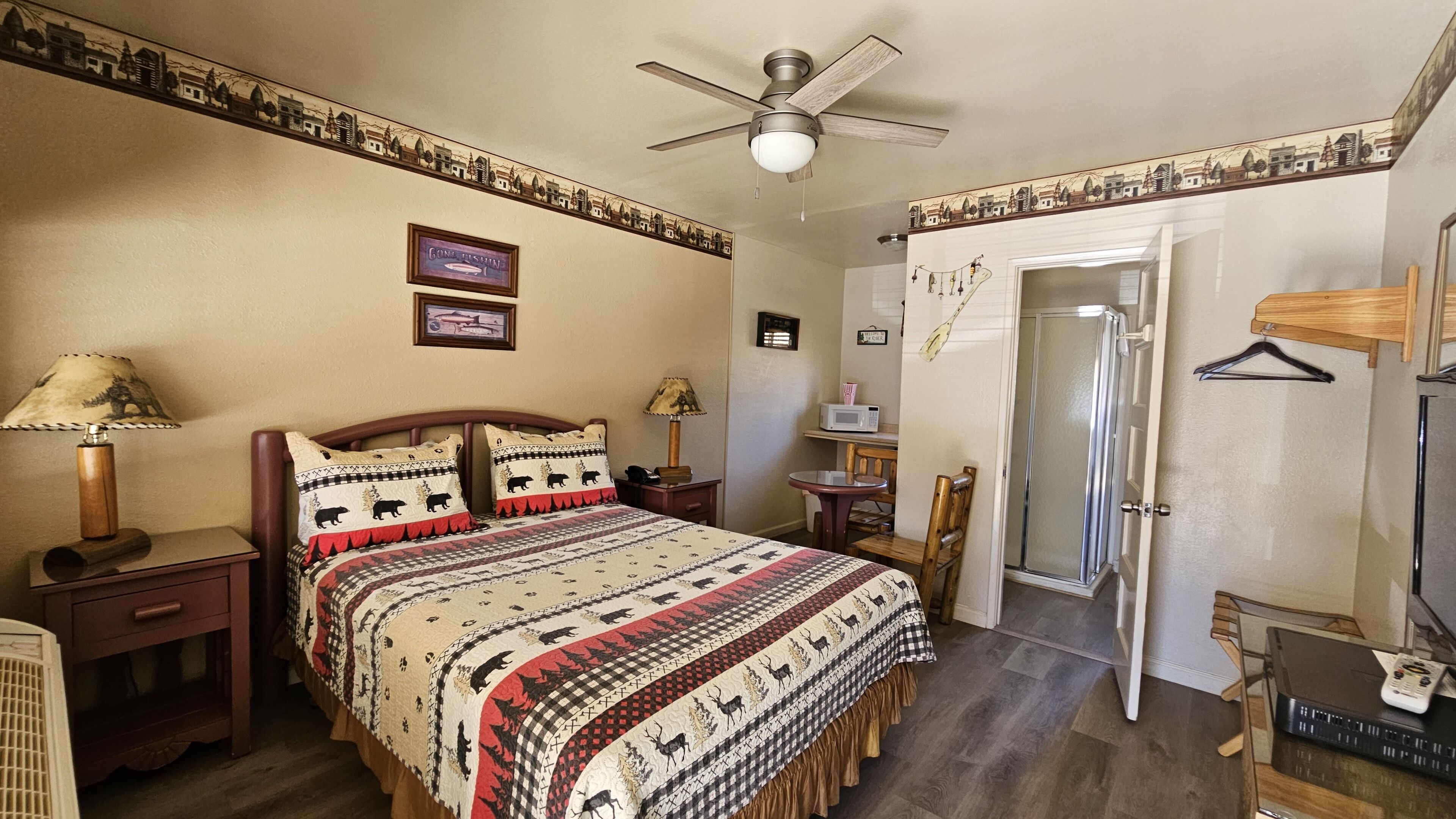 Ein Schlafzimmer mit Bett, Nachttischlampen, Schreibtisch, Stuhl, Tür und Deckenventilator.