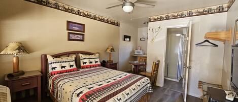 Ein Schlafzimmer mit Bett, Nachttischlampen, Schreibtisch, Stuhl, Tür und Deckenventilator.