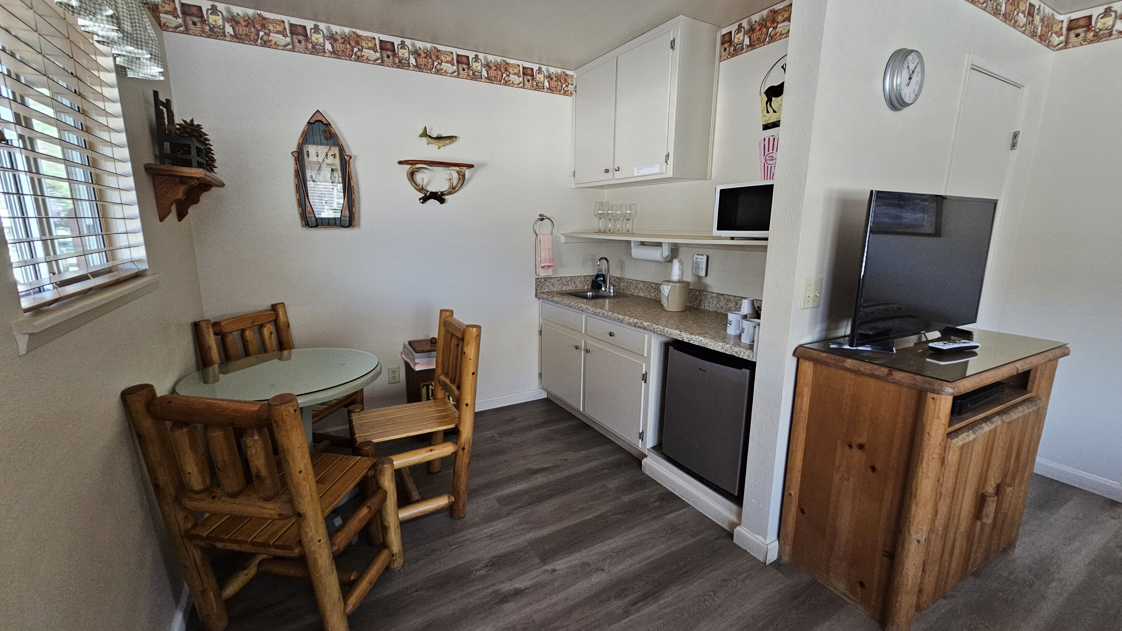 A compact kitchen with a dining table and chairs, a built-in dishwasher, and a small wooden cabinet with a television.