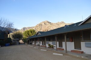 Un motel con un área de estar al aire libre techada, un camino de entrada de grava y montañas al fondo.