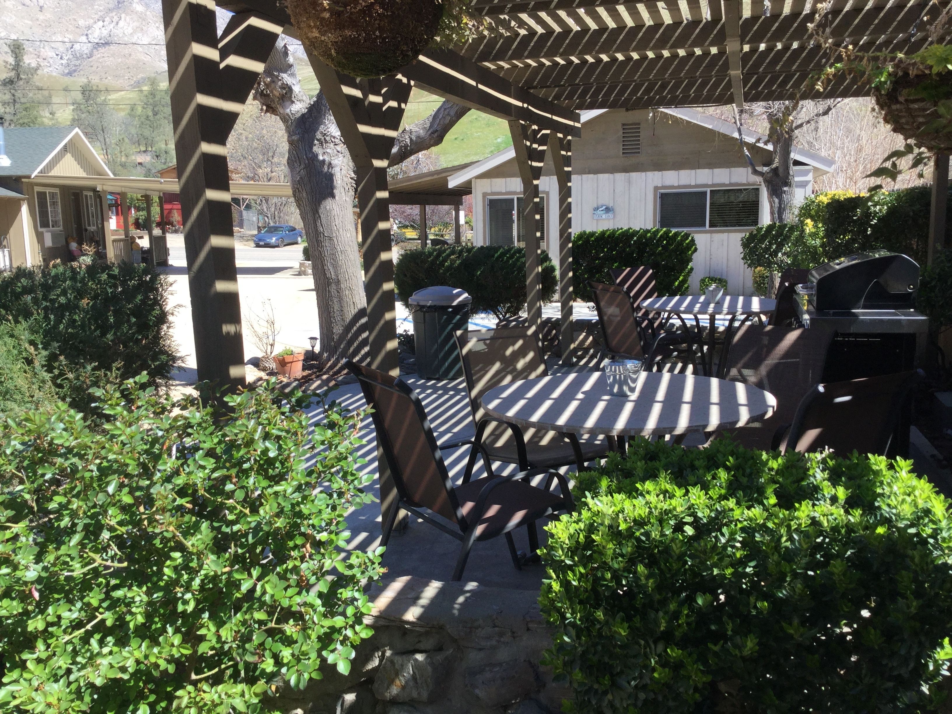 An outdoor patio with a pergola, round tables, and chairs.