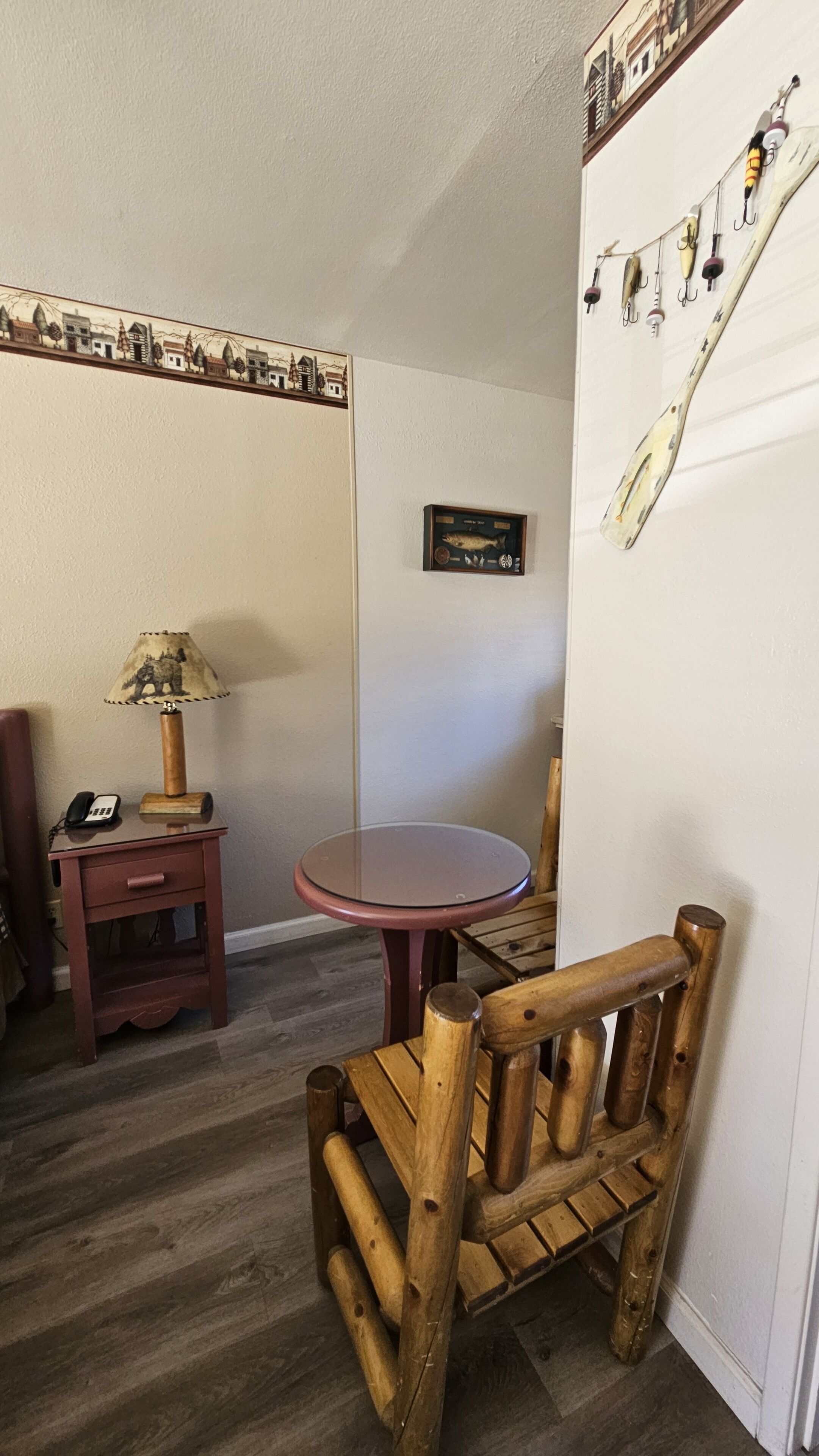 A wooden chair, a small table, a lamp, a phone, and a wall with fishing lures and a fish plaque.
