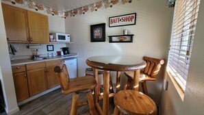 Una cocina con armarios de madera, microondas, cafetera y comedor con mesa redonda y sillas de madera.