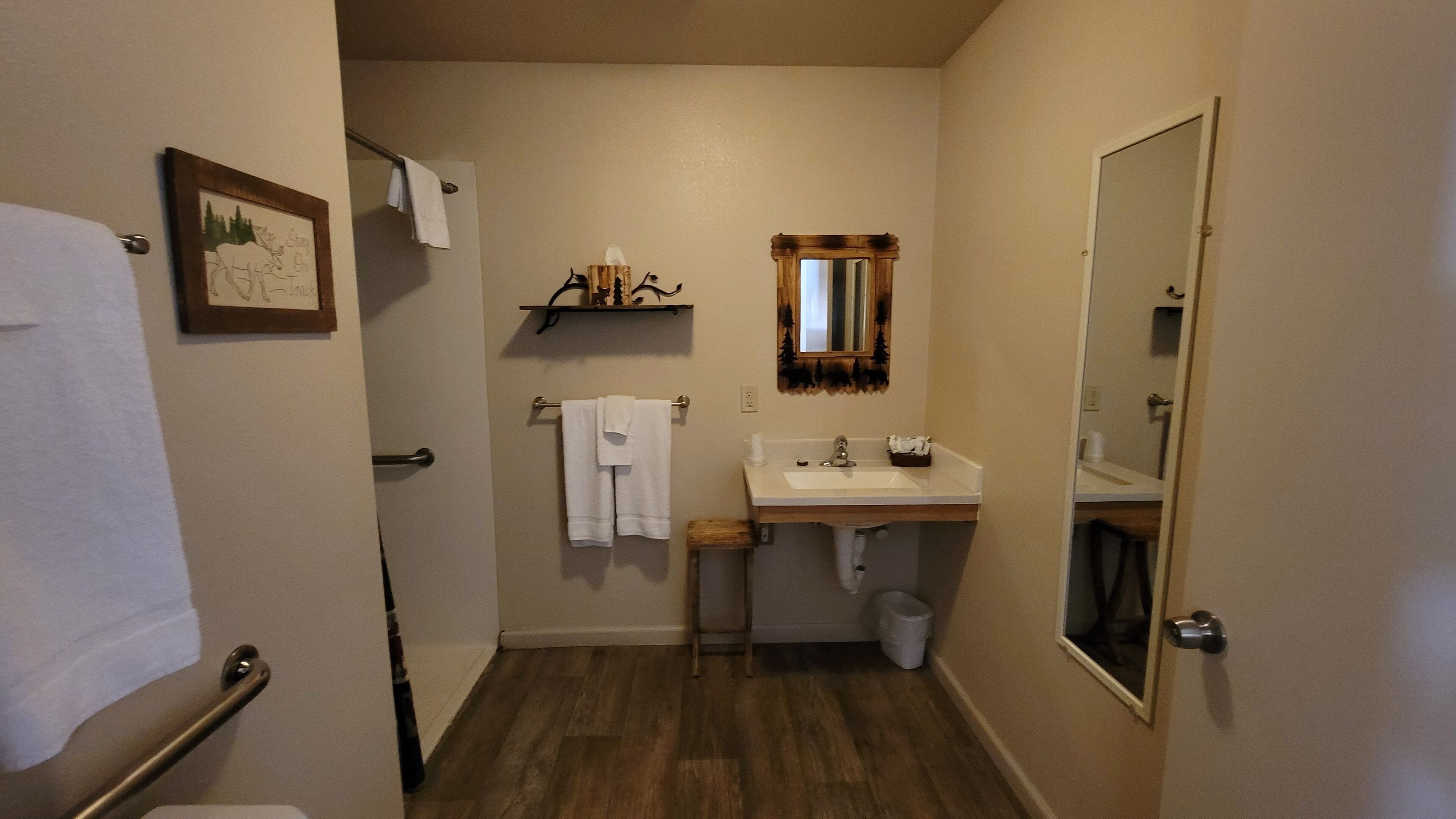 Un baño con piso de madera, un lavamanos blanco, un espejo y un perchero para toallas.
