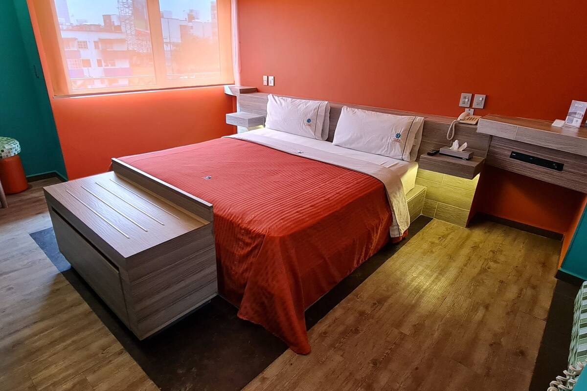 Ein modernes Hotelzimmer mit Bett, Nachttisch und einem kleinen Tisch mit Stühlen.