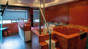 Een moderne badkamer met een rode betegelde jacuzzi, een douchecabine met glazen wanden en een zithoek met een bankje en poef.