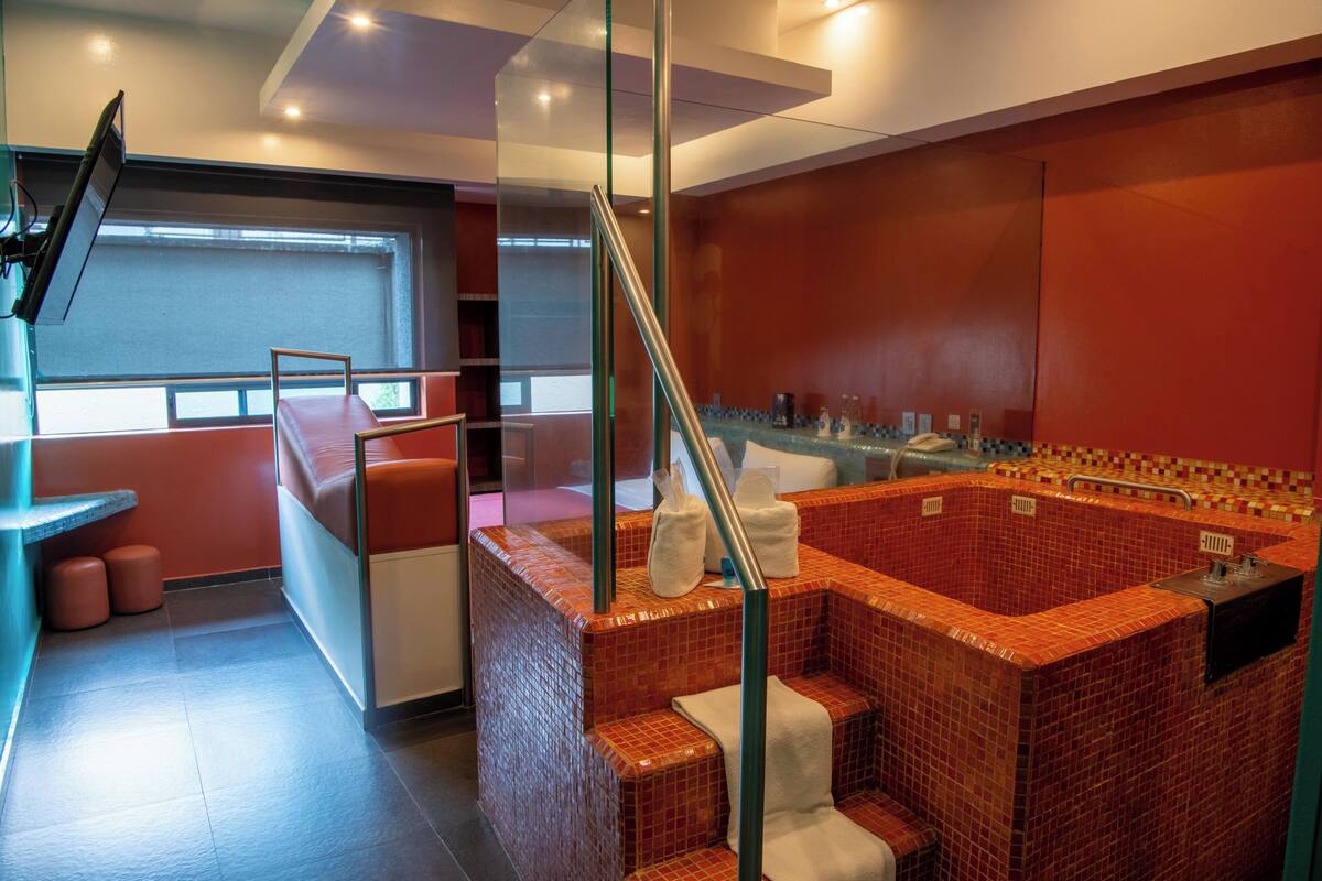 Ein modernes Badezimmer mit einem jacuzzi mit roten Fliesen, einer gläsernen Duschkabine und einer Sitzecke mit einer Bank und Hocker.