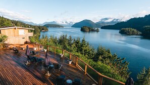 Una terraza de madera con mobiliario exterior que da a un lago y montañas.