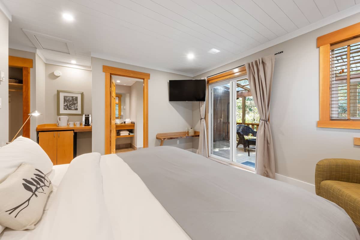 Camera da letto con un letto grande, una TV montata a parete, una scrivania in legno e una porta scorrevole in vetro che dà su uno spazio esterno.