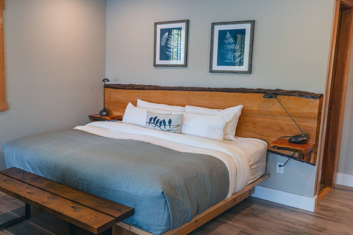 Una camera da letto con un letto di legno, un comodino, una lampada da notte, una panca e due quadri appesi al muro.