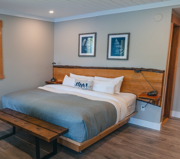 Un dormitorio con una cama de madera, una mesita de noche, una lámpara de noche, un banco y dos cuadros en la pared.