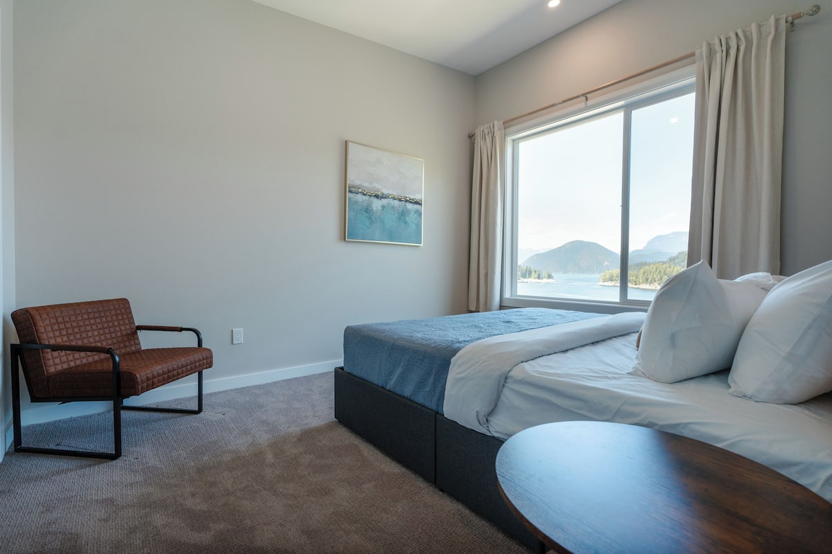 Una camera da letto con un letto, una sedia, una finestra vista e un quadro appeso al muro.