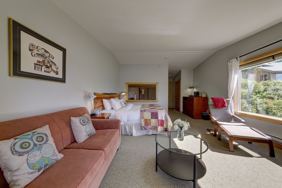 Una camera d'albergo con un letto, un divano, una sedia, una scrivania e una finestra vista verde.