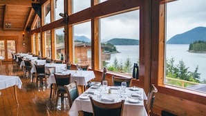 En restaurang med träinredning och stora fönster som erbjuder utsikt över en sjö och berg.