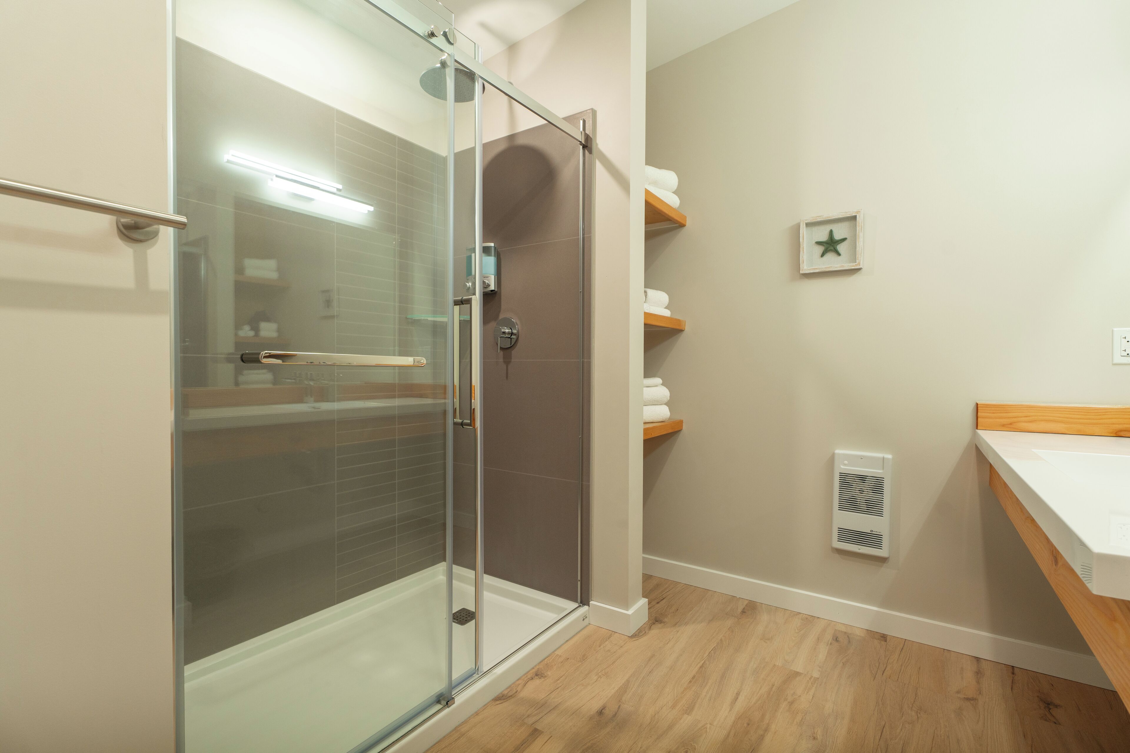 A modern bathroom with a glass shower enclosure, wooden flooring, a white sink, and a towel rack.