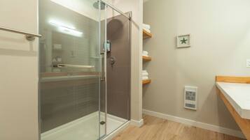 A modern bathroom with a glass shower enclosure, wooden flooring, a white sink, and a towel rack.