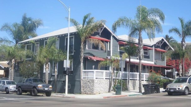 Un edificio de dos plantas con techo rojo y barandillas blancas, rodeado de palmeras.