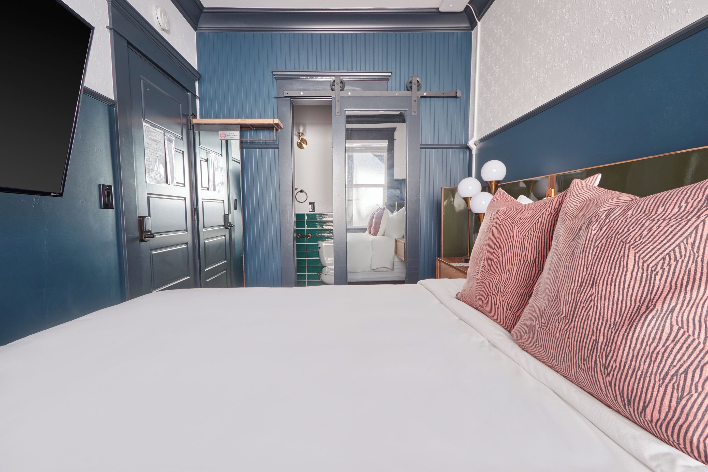 Une chambre avec un grand lit, une porte coulissante donnant accès à une salle de bain et un miroir avec un cadre doré.