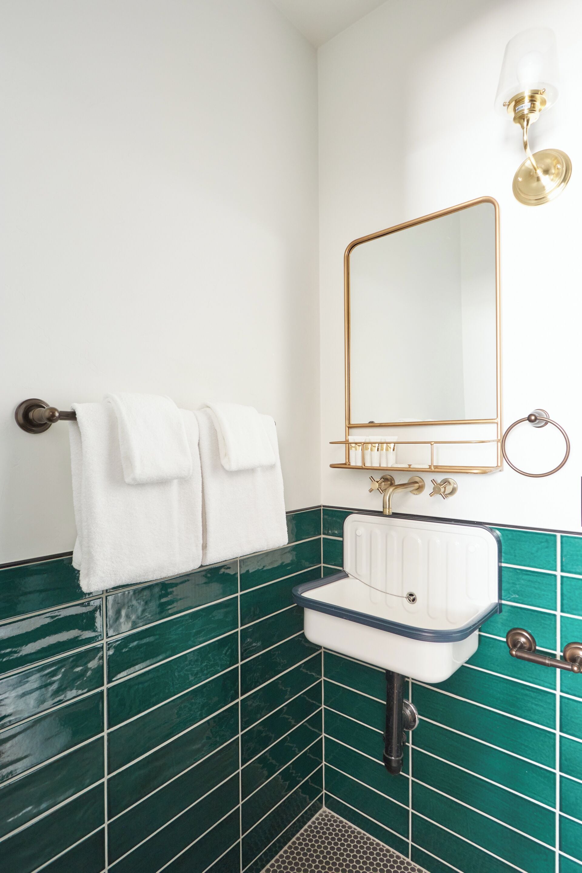 A bathroom with a white sink, green tiled walls, a gold-framed mirror, and a towel rack with white towels.