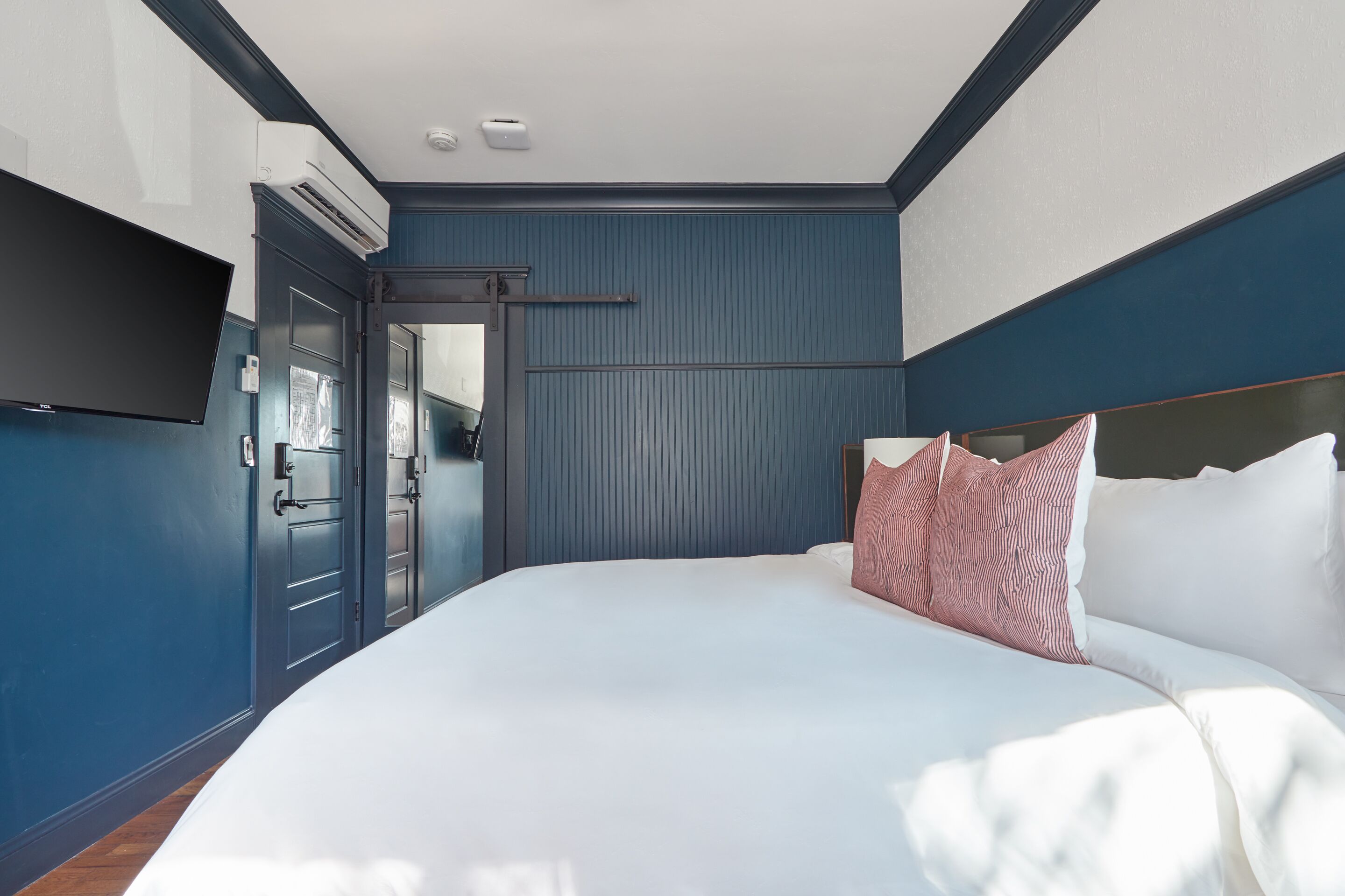 Een slaapkamer met een groot bed, een flatscreen televisie aan de wand en een deur naar een andere kamer.