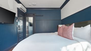 Een slaapkamer met een groot bed, een flatscreen televisie aan de wand en een deur naar een andere kamer.