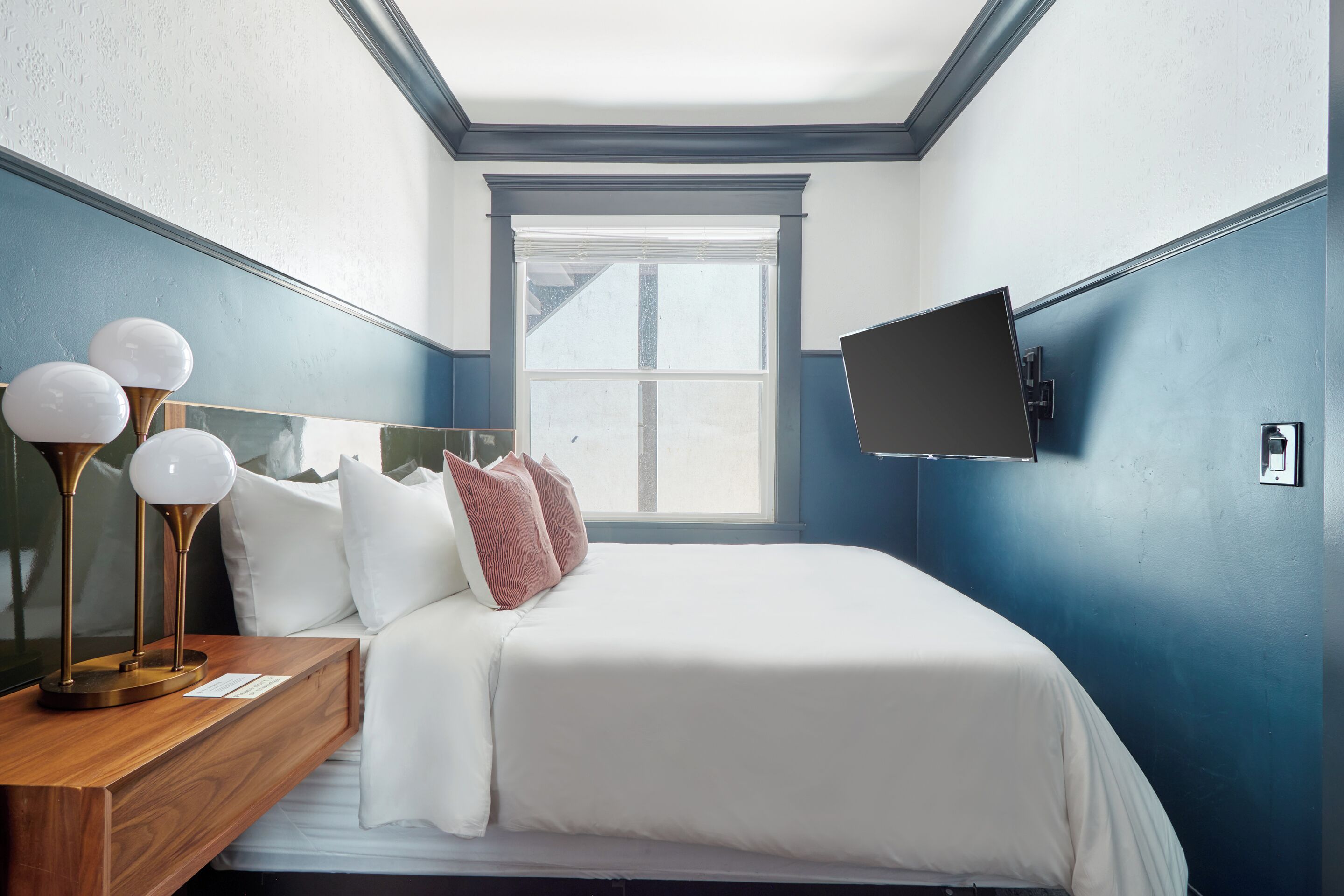 A bedroom with a large bed, a bedside table with a lamp, and a TV mounted on the wall.