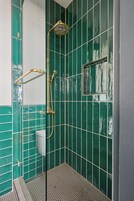 Un baño con paredes de azulejos verdes, ducha con ducha dorada y un inodoro.